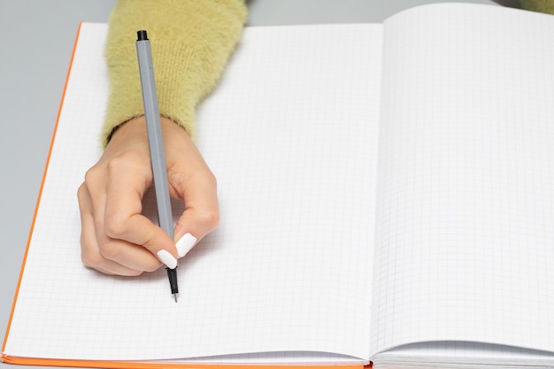 Mão feminina com um marcador que escreve em uma página de caderno vazia