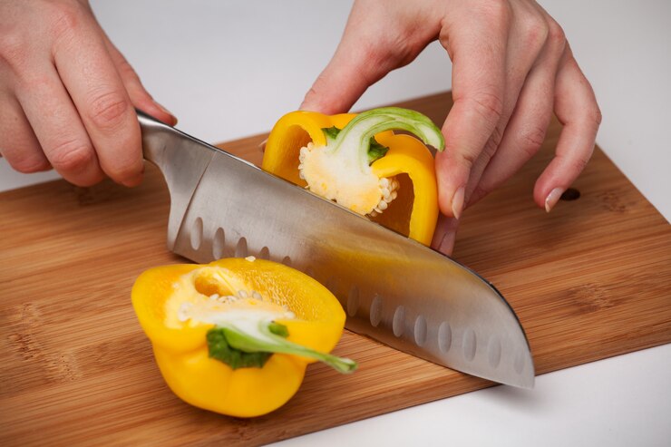 Foto mão feminina com uma faca de cozinha, corte o pimentão amarelo sobre uma tábua de madeira