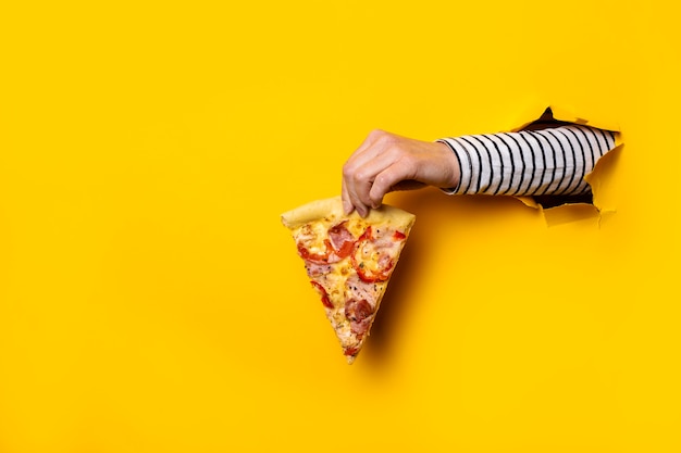 Foto mão feminina com uma fatia de pizza quente fresca em um rasgado