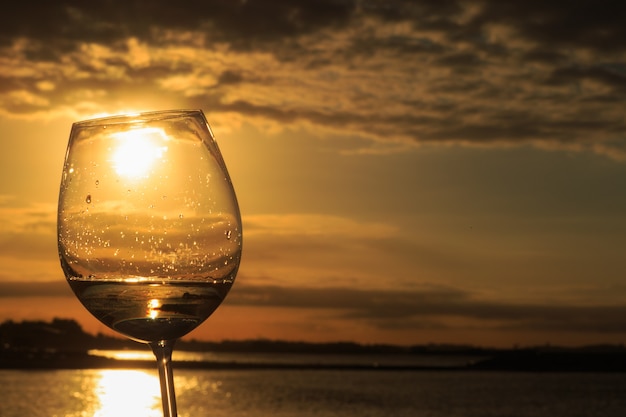 Mão feminina com uma taça de vinho branco com lindo pôr do sol