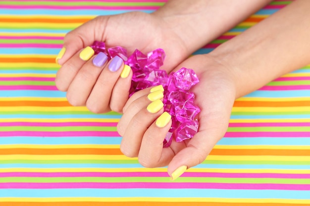 Foto mão feminina com unhas coloridas elegantes segurando pedras decorativas em fundo brilhante