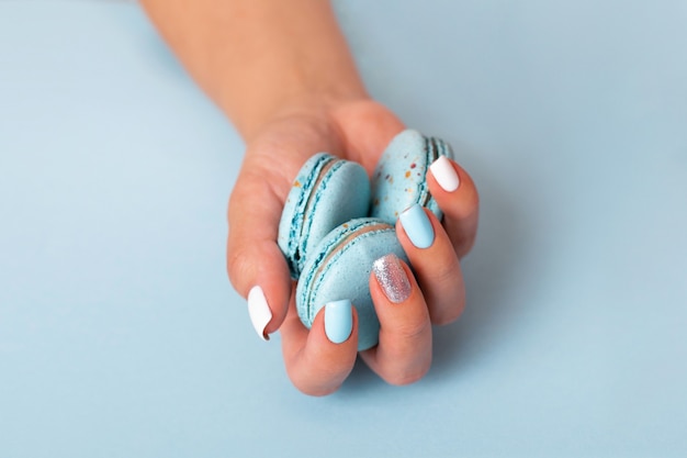 Mão feminina com unhas manicure azuis segurando macaroons doces