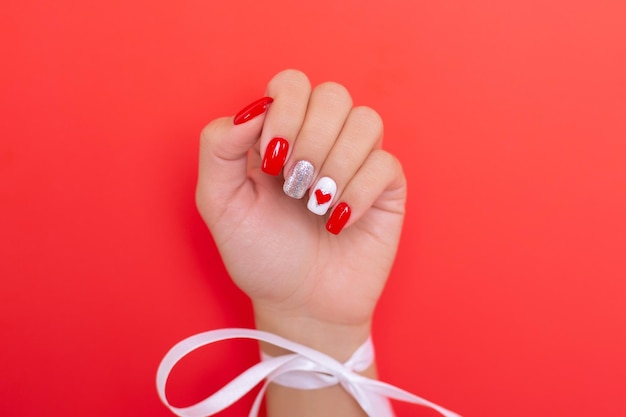 Mão feminina com unhas vermelhas de manicure, desenho de coração