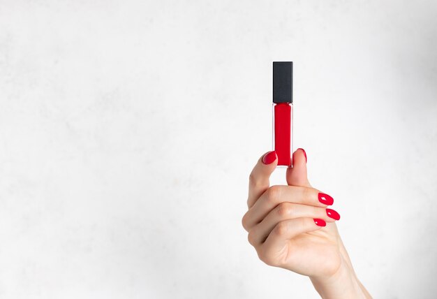 Mão feminina com unhas vermelhas segurando batom líquido vermelho