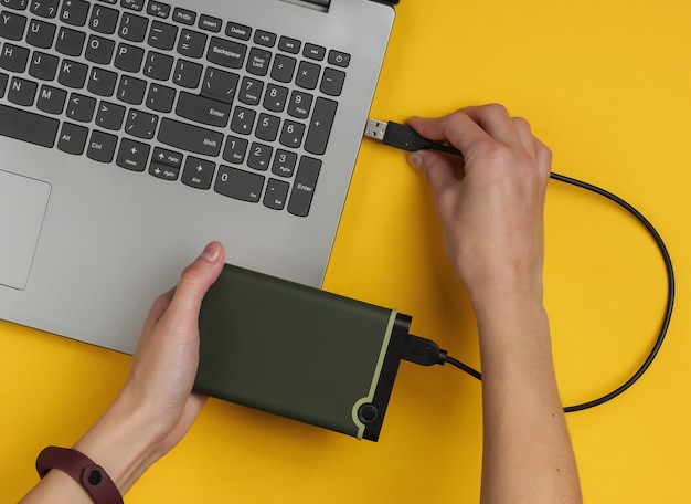 Foto mão feminina conecta-se externamente a um laptop em papel amarelo
