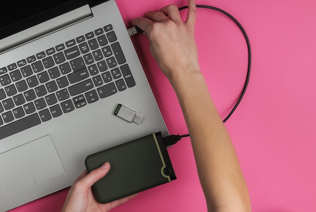 Mão feminina conectada externamente a um laptop em papel rosa