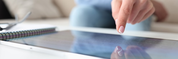 Mão feminina cutucando o dedo na tela do conceito de educação doméstica de tablet digital closeup