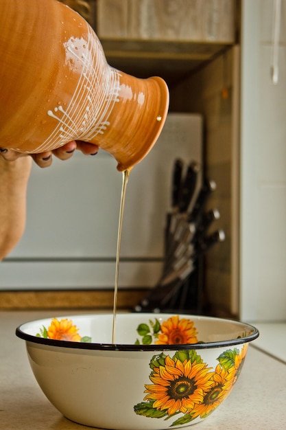 Foto mão feminina derramando óleo de ewer de cerâmica em uma tigela de metal pintada em esmalte branco uma jarra de barro marrom closeup massa de cozinha vertical