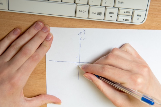 Mão feminina desenha um eixo para plotagem, lição de matemática, close-up. Conceito de ensino em casa