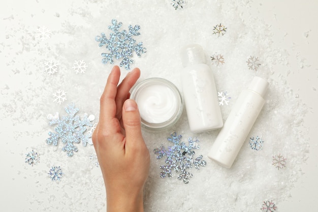 Mão feminina e cosméticos em fundo com neve decorativa