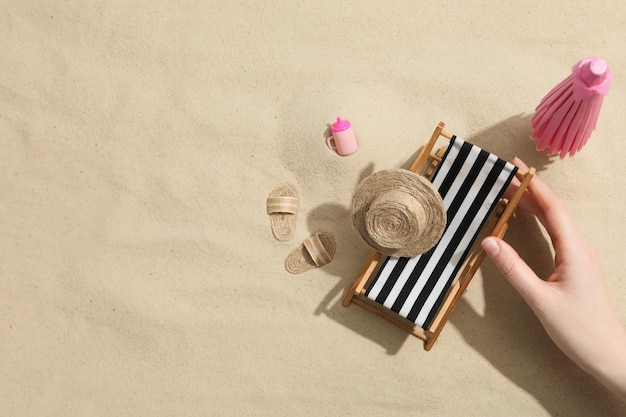 Mão feminina e mini acessórios de praia em fundo de areia