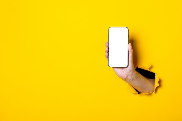 Mão feminina em um fundo amarelo segurando um telefone vertical, tela branca