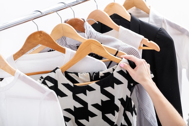 Mão feminina escolhe novas roupas da moda em cabides de madeira na prateleira em fundo branco, closeup. Conceito de compras