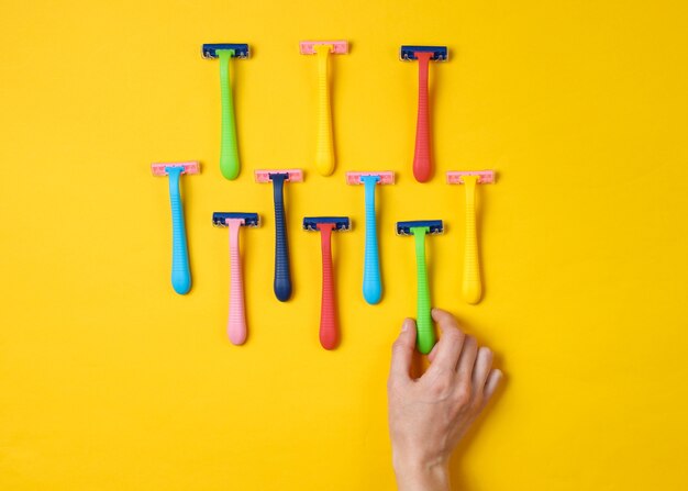 Mão feminina escolhendo uma lâmina de barbear entre uma variedade de lâminas de depilação coloridas em amarelo. Vista do topo. Conceito de beleza minimalista