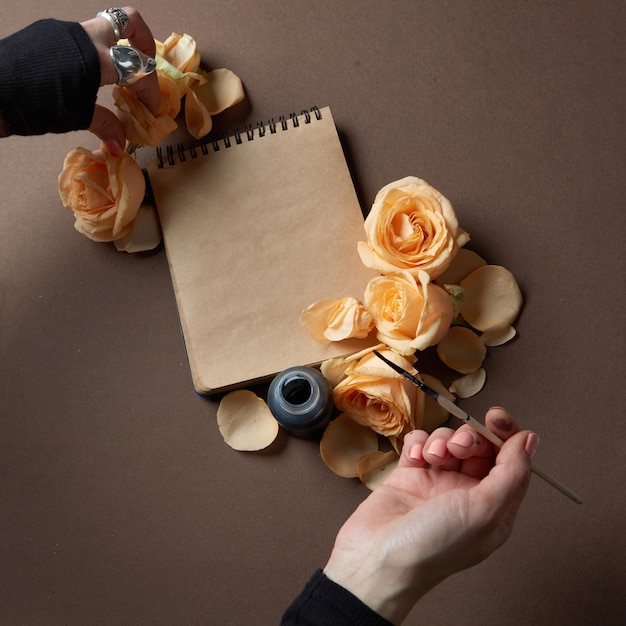 Mão feminina escrevendo em papel de carta com flores na mesa da sobrancelha, vista superior