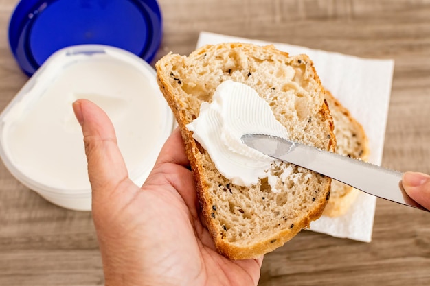 Mão feminina espalhando queijo branco em uma fatia de pão em uma mesa de madeira