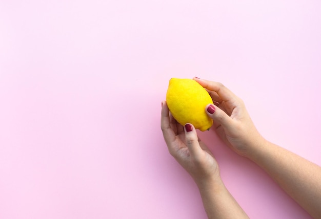 Mão feminina jovem segurando limão em fundo rosa pastel.frutas e ideias de conceitos saudáveis