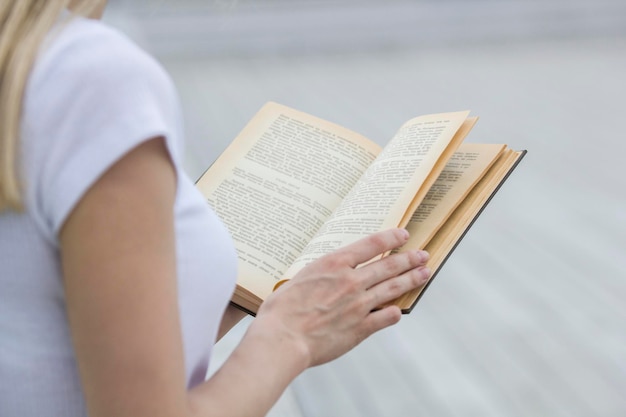 Mão feminina jovem segurando um livro antigo - lendo ao ar livre, close-up