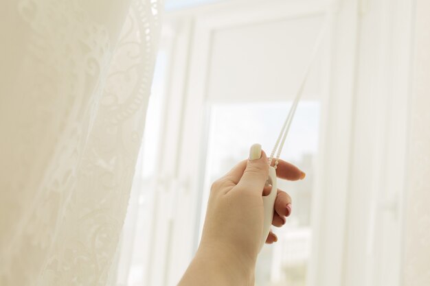 Mão feminina levantando as cortinas de uma janela de plástico