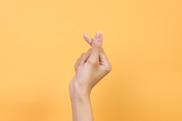 Mão feminina mostrando mini coração coreano de dedos sobre fundo amarelo