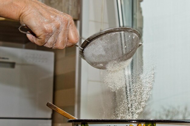 Foto mão feminina peneirando farinha através de peneira manual de farinha em uma tigela cópia de close-up espaço de cozimento de massa utensílio de cozinha de metal