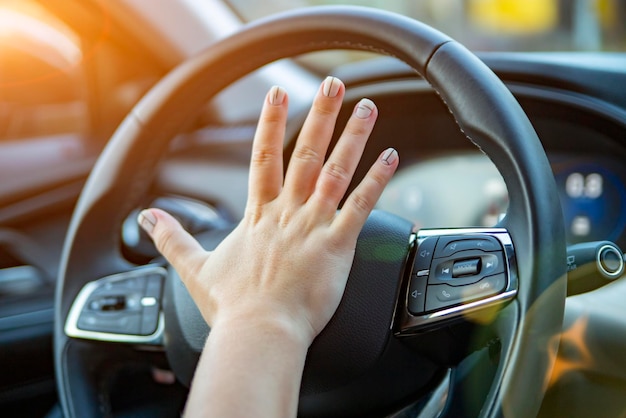 Mão feminina pressiona a buzina no volante de um carro moderno sem rosto
