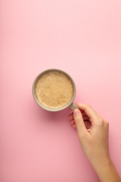 Mão feminina segura a xícara de café no fundo rosa
