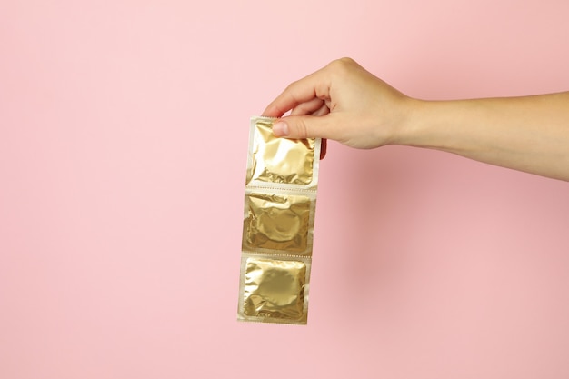 Foto mão feminina segura preservativos em fundo rosa, espaço para texto