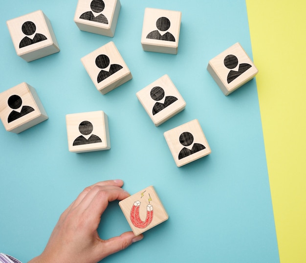 Foto mão feminina segura um cubo de madeira com um ímã e cubos de madeira com homenzinhos, recrutando para uma equipe forte. vagas abertas na empresa, flat lay