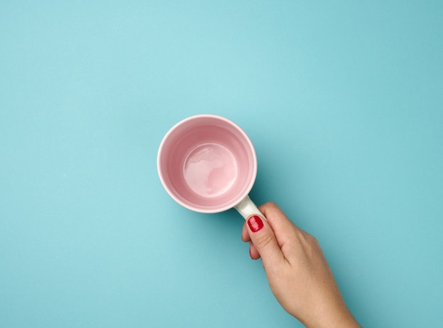 Mão feminina segura uma caneca de cerâmica cinza vazia sobre um fundo azul, hora do intervalo e bebe café, vista de cima