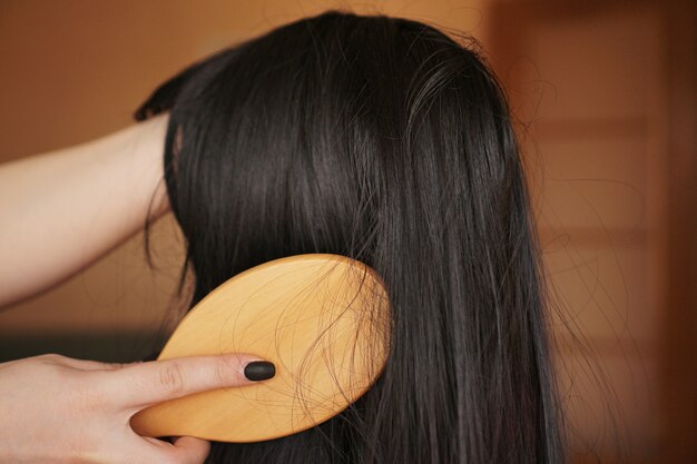 Mão feminina segura uma peruca preta com cabelo comprido e penteia um pente de madeira. cabeleireiro e cuidados com os cabelos