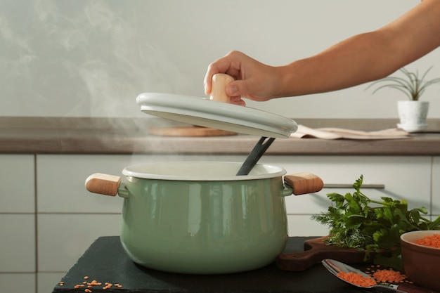 Mão feminina segurando a tampa acima da panela esmaltada na cozinha