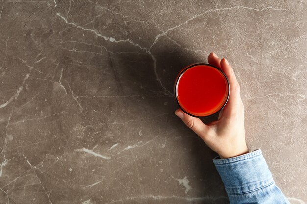 Mão feminina segurando copo de suco de tomate em cinza