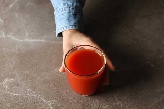 Mão feminina segurando copo de suco de tomate em fundo cinza