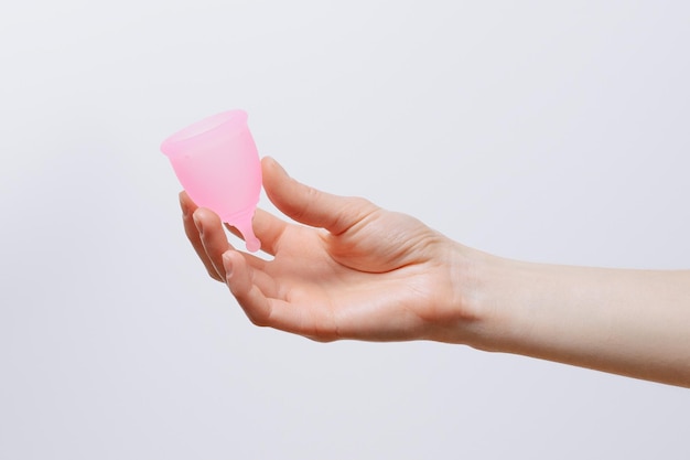 Mão feminina segurando copo menstrual rosa em fundo branco isolado Produtos de higiene ciclo menstrual feminino e conceito alternativo ecológico