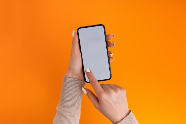 Mão feminina segurando e tocando no smartphone móvel com tela branca isolada no modelo de foto laranja para qualquer imagem no layout de exibição do telefone móvel com fundo de monitor de telefone facilmente removível