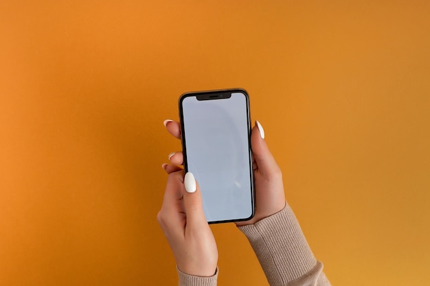 Mão feminina segurando e tocando no smartphone móvel com tela branca isolada no modelo de foto laranja para qualquer imagem no layout de exibição do telefone móvel com fundo de monitor de telefone facilmente removível