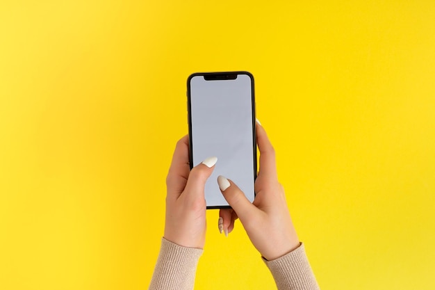Mão feminina segurando e tocando no smartphone móvel com tela branca Isolado em amarelo Modelo de foto para qualquer imagem no visor do celular Layout com fundo de monitor de telefone facilmente removível