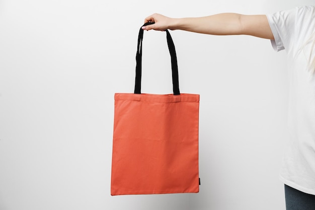Mão feminina segurando eco ou sacola de compras reutilizável contra fundo branco