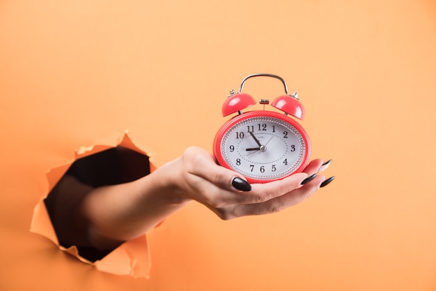 Mão feminina segurando o despertador em fundo laranja