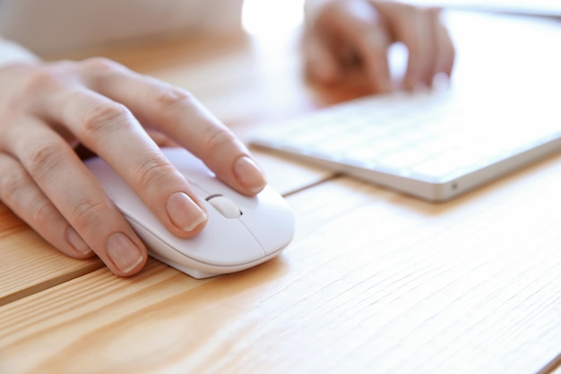 Mão feminina segurando o mouse do computador na mesa de madeira