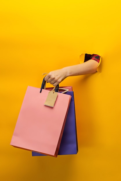 Mão feminina segurando sacolas de compras brilhantes em amarelo