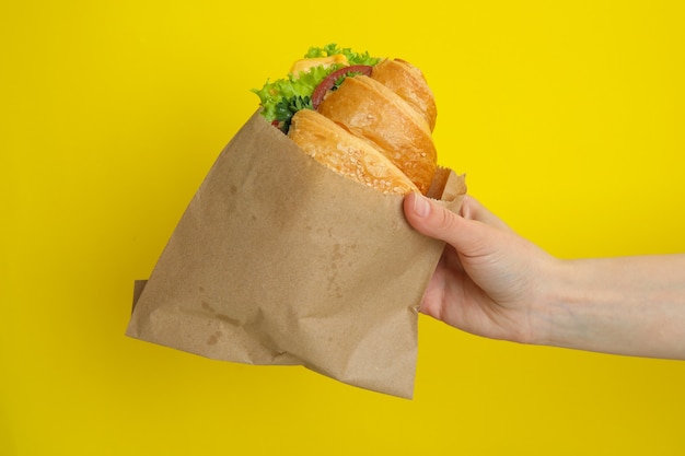 Foto mão feminina segurando sanduíche de croissant em amarelo