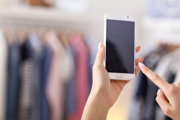 mão feminina segurando smartphone em loja de roupas