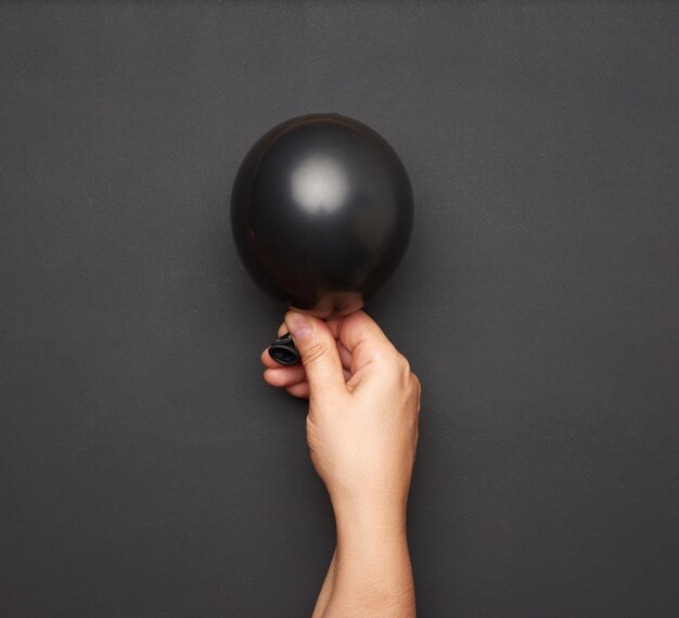 Foto mão feminina segurando um balão de ar preto inflado em um fundo preto de perto
