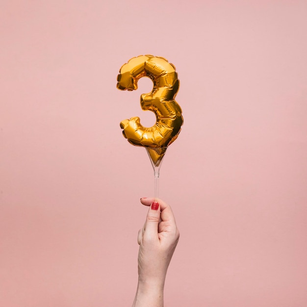 Mão feminina segurando um balão de ouro de comemoração de aniversário de aniversário de número
