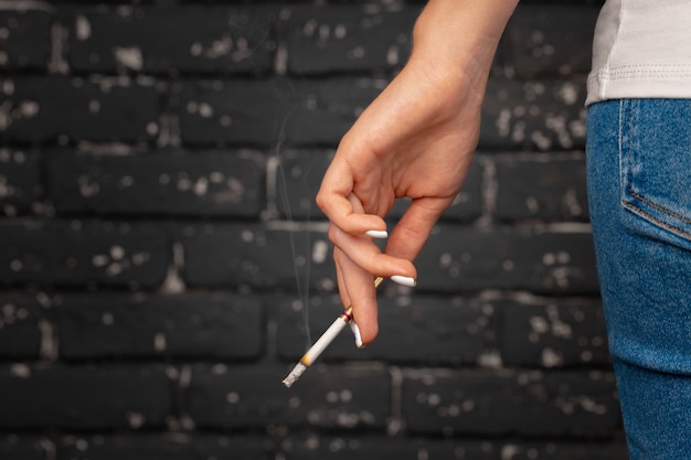 Mão feminina segurando um cigarro aceso de perto