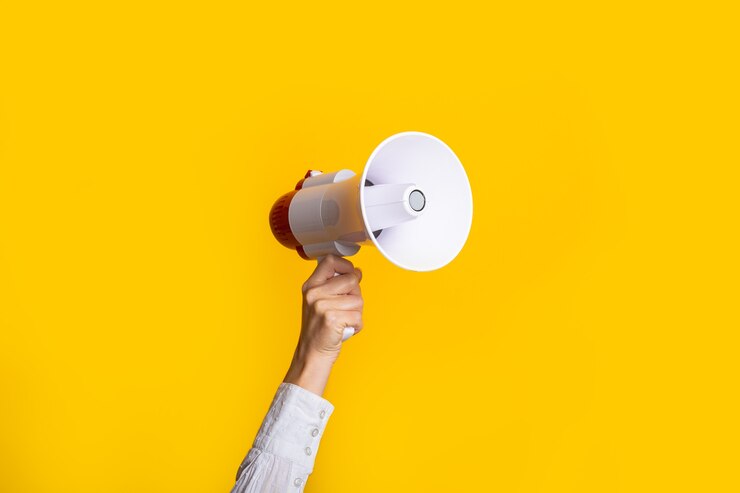 Foto mão feminina segurando um megafone branco em um fundo amarelo