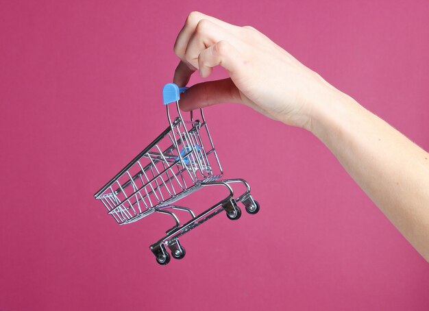 Mão feminina segurando um mini carrinho de compras sobre fundo vermelho. conceito de compras