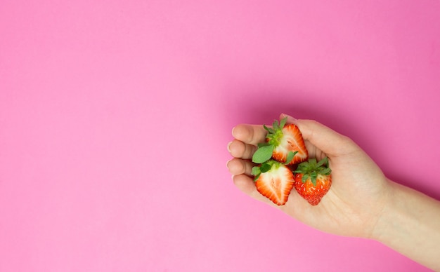 Mão feminina segurando um morango no fundo rosa. Faixa plana leiga. Espaço para texto. Resumo.